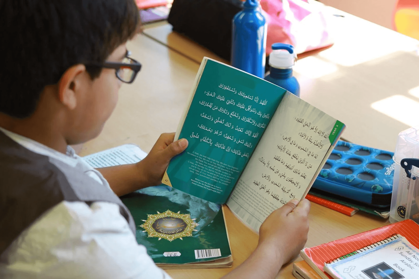 A pupil reading an Arabic du‘ā book at his desk