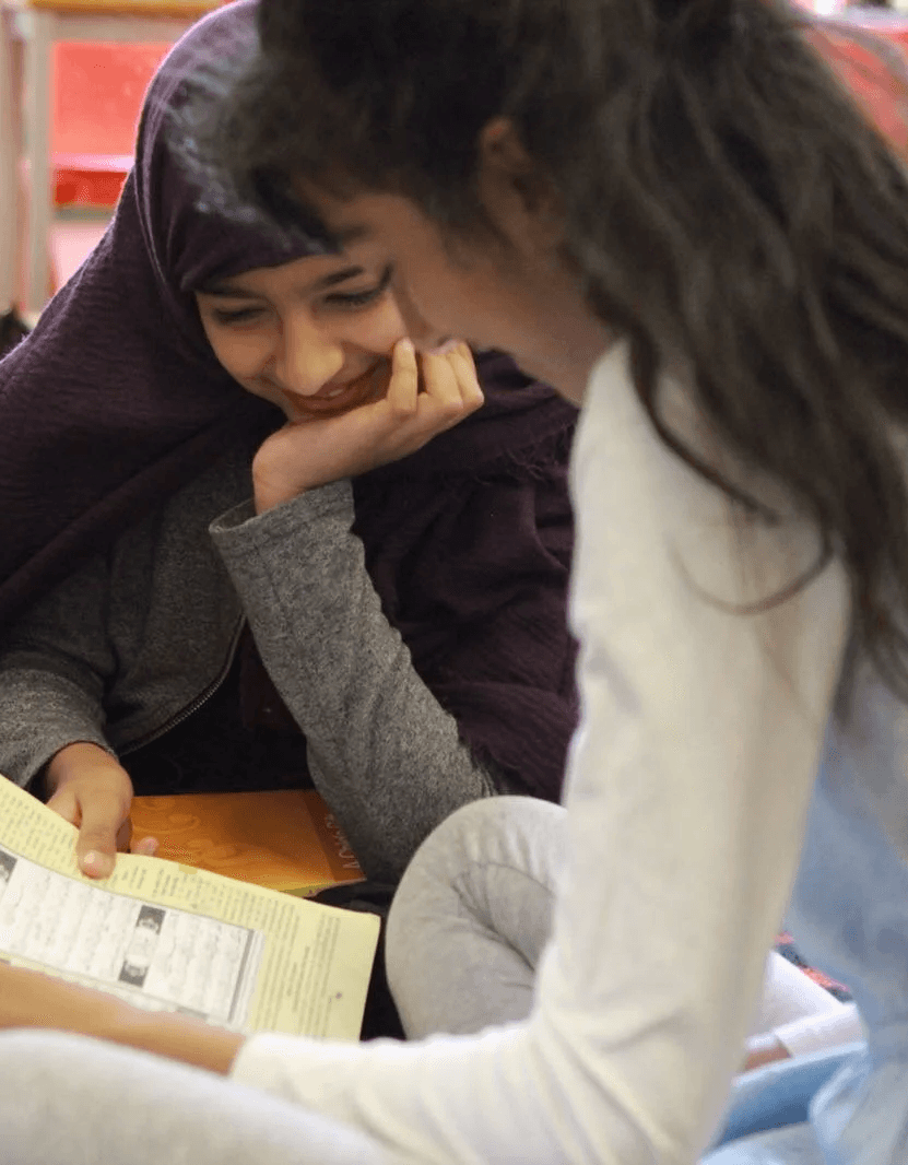 Two pupils reading together, one smiling at the other